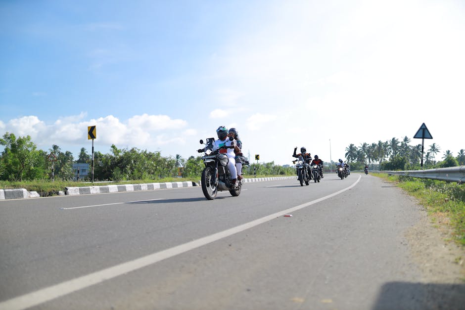 A group of motorcyclists riding together on a sunny highway with vegetation in the background.