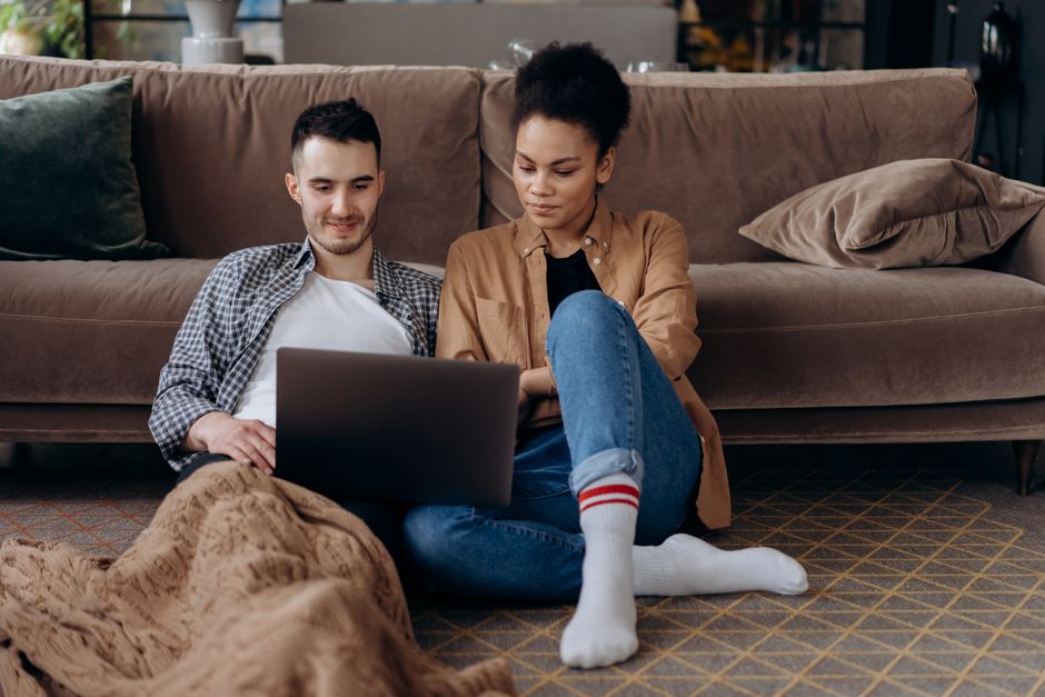 Couple sitting on the floor, using a laptop for entertainment at home.