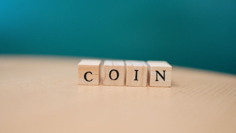 Wooden blocks arranged to spell 'coin' on a wooden surface against a teal background.
