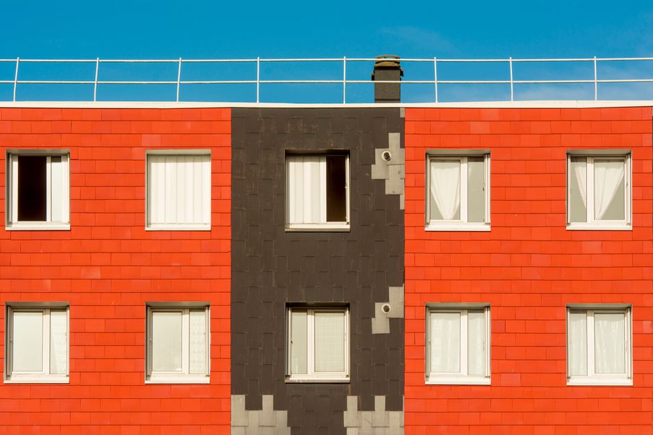 Colorful modern apartment facade with windows, featuring vivid red and black panels under a clear blue sky.