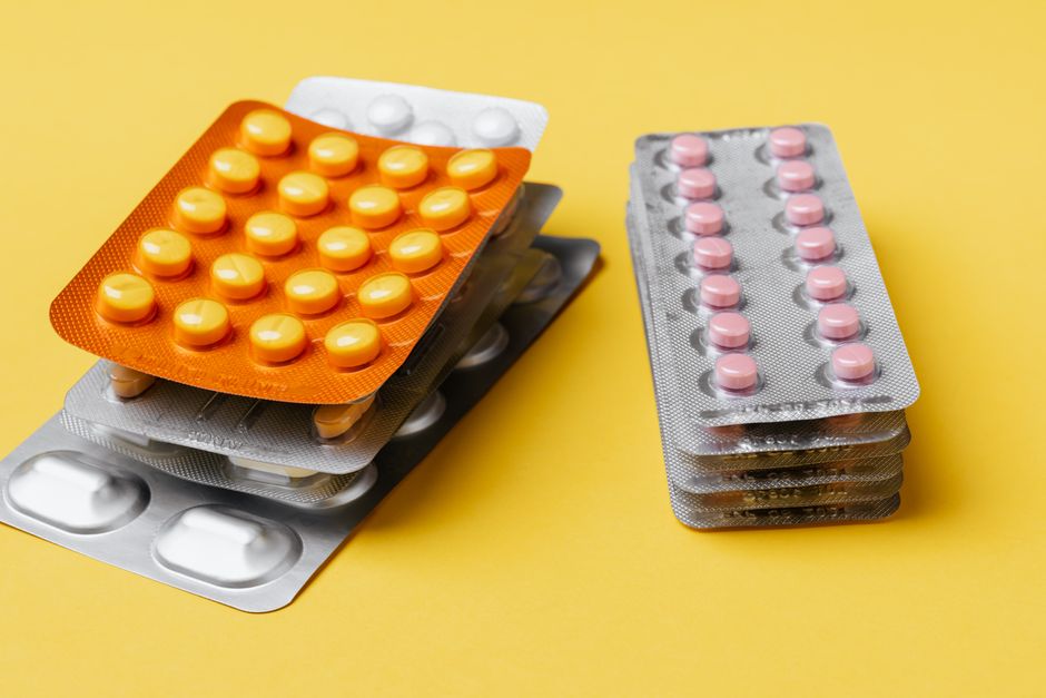 Heaps of various medication pills of different color and shape in blister packs placed on bright yellow background