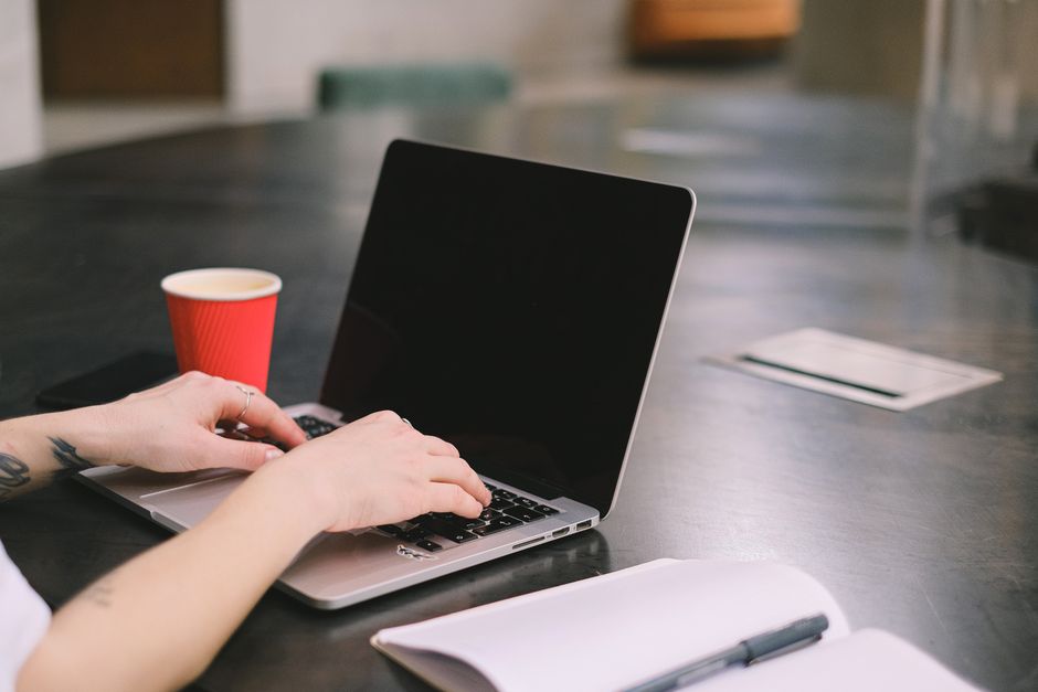 A freelancer typing on a laptop with a coffee cup nearby in a modern office setting.