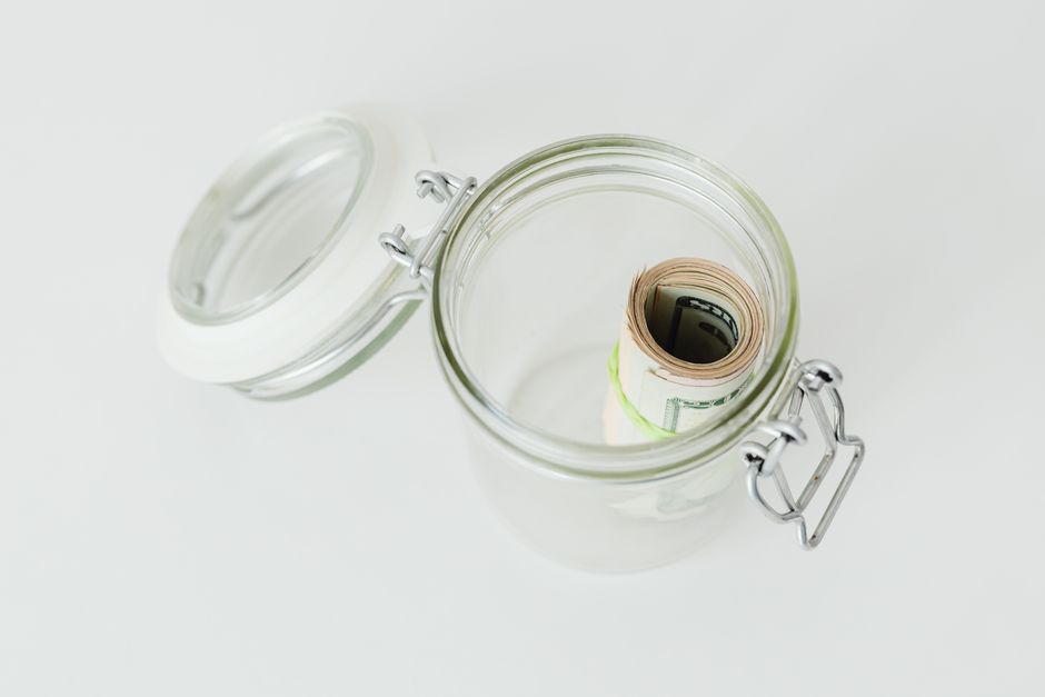 Close-up shot of rolled US dollar bills inside a glass jar on a white surface.