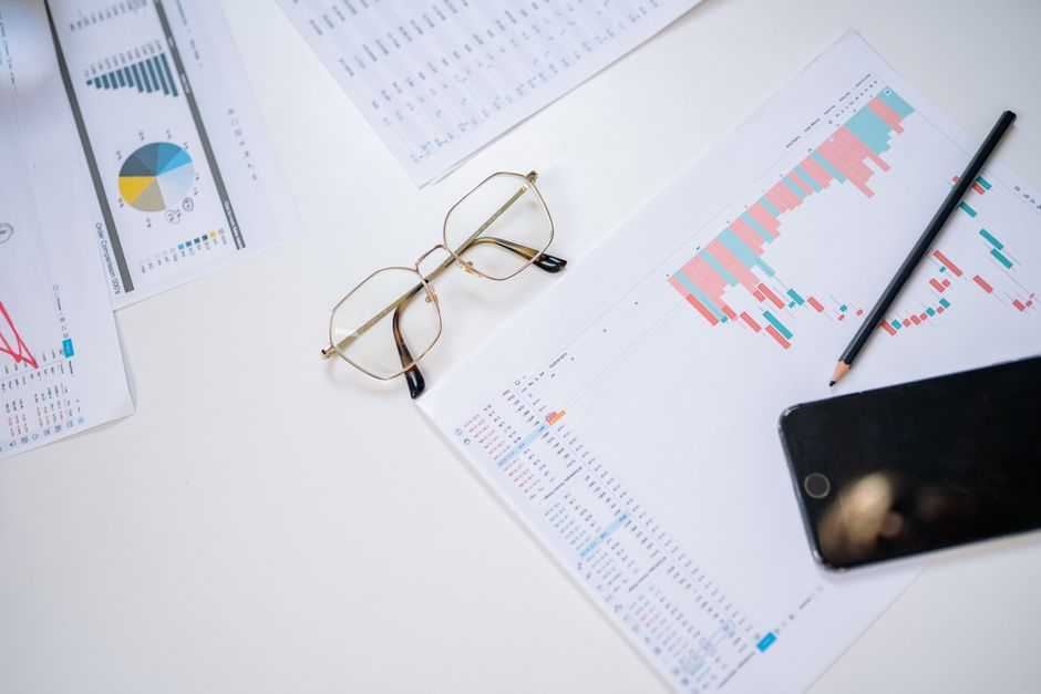 A high-angle view of business charts with eyeglasses, smartphone, and pencil on a white background.