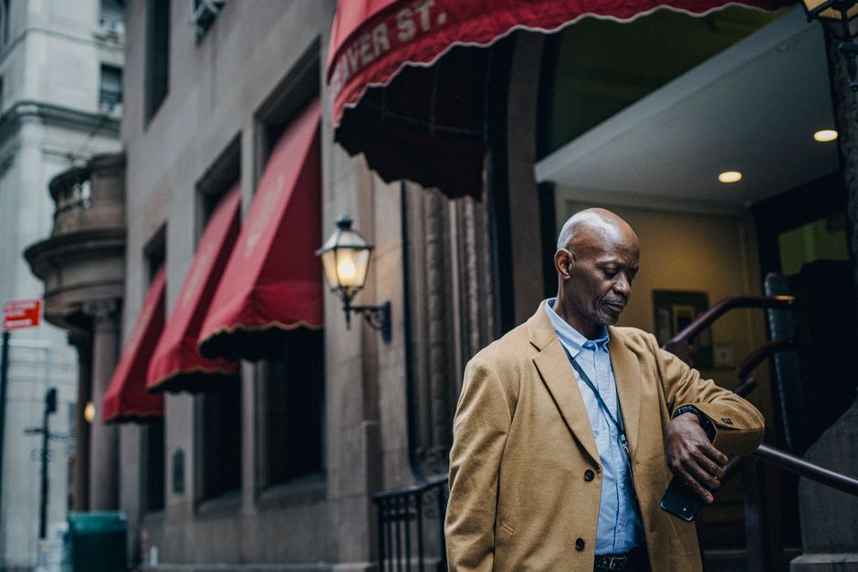 Confident African American man in trendy clothes standing on street near entrance of building and looking at watch while checking time